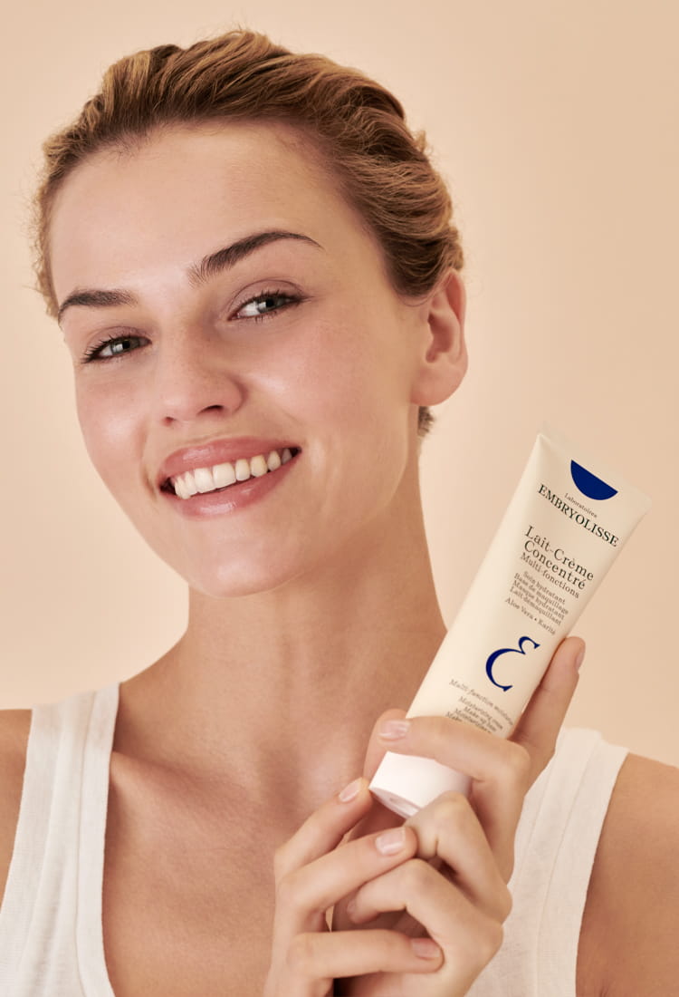 Woman holding a skincare product with a beige background