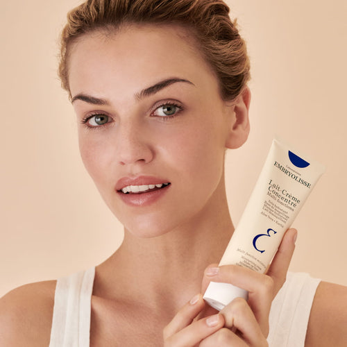 Woman holding a skincare product with a beige background